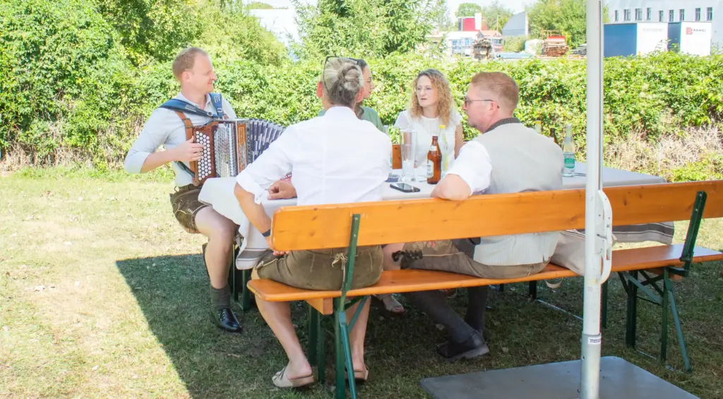 Mitglieder des Gewerbevereins sitzen zusammen und ein Mann spielt Akkordeon.
